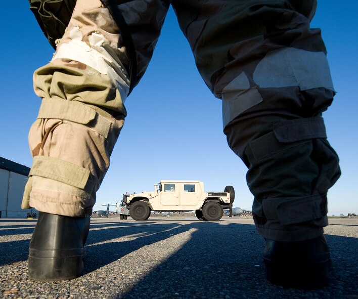The legs of Staff Sgt. Nicholas Sbano, 436th Aerial Port Squadron, frame a HUMMVEE driving near the flightline during an evaluation of personnel to perform their duties wearing full chemical protective gear Dec. 13, 2012, at Dover AFB, Del. On each side of the HUMMVEE are the two different aircraft types operated by the 436th Airlift Wing; a C-17A Globemaster III and a C-5M Galaxy. The 436th Maintenance Group conducted a training exercise to evaluate the deployment preparedness levels of its Airmen. (U.S. Air Force photo by Greg L. Davis)