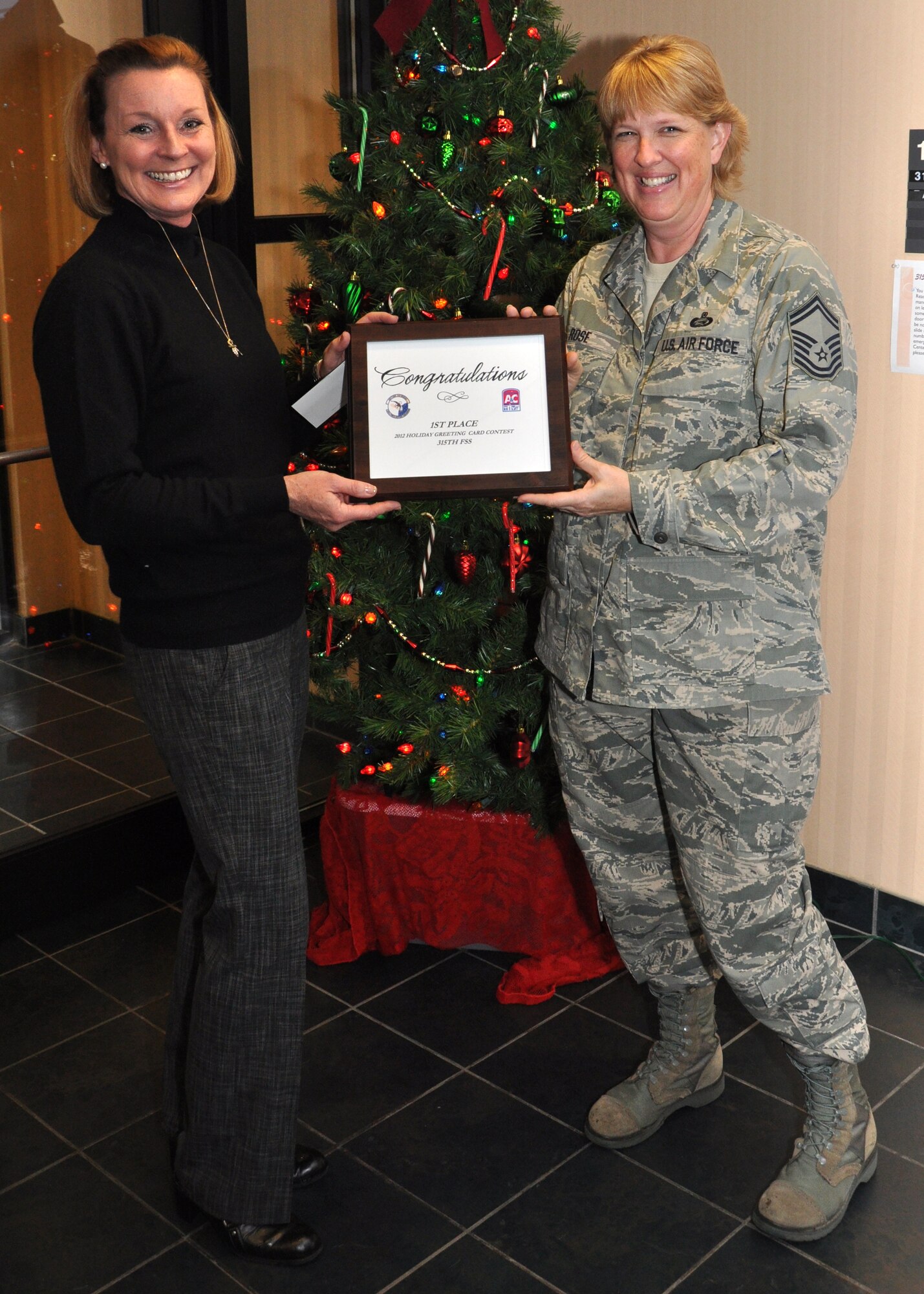 Senior Master Sgt. Karla Rose accepts the 2012 Air Base Holiday Card contest award presented to her by Beverley McElroy Dec. 11, 2012 at Joint Base Charleston, S.C. Rose helped lead the 315th Airlift wing to victory in this year’s card competition by joining forces with Airmen, friends and neighborhood kids. Rose is the 315th Force Support Squadron superintendent, and McElroy is the 628th FSS special events coordinator. (U.S. Air Force photo/Staff Sgt. Shane Ellis)