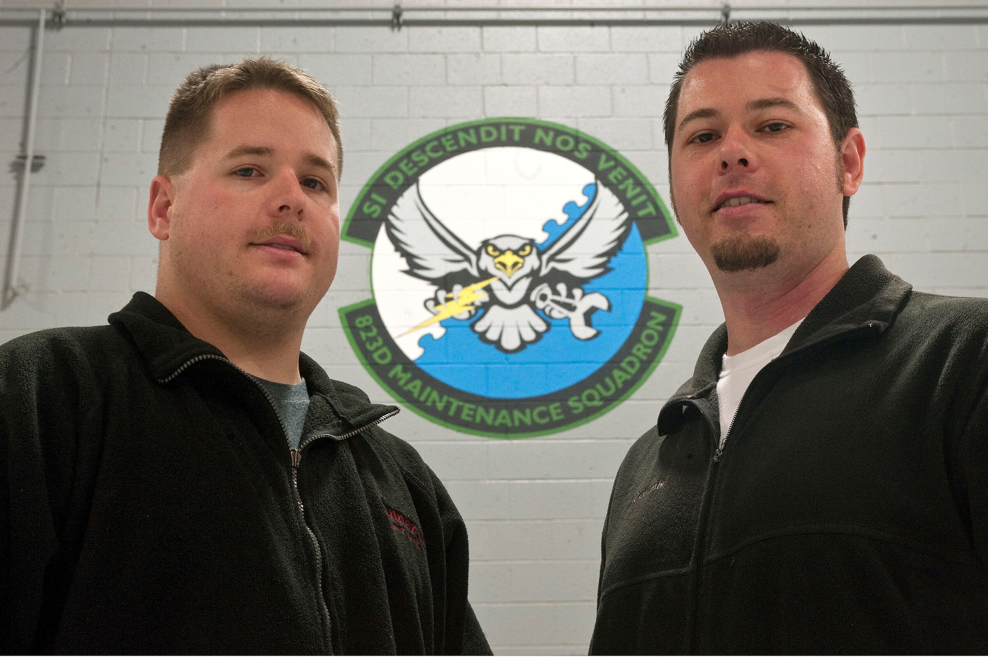 Staff Sgt. Daniel Sullivan, 823rd Maintenance Squadron aircraft structural maintenance craftsman, and Michael Sullivan, artist and brother of Sergeant Daniel Sullivan, pose in front of the new 823rd MXS unit patch Dec. 15, 2012, at Nellis Air Force Base, Nev. The brothers were able to paint the patch in less than 12 hours. (U.S. Air Force photo by Staff Sgt. Christopher Hubenthal)