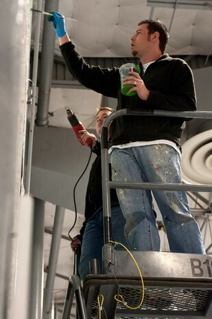 Staff Sgt. Daniel Sullivan, 823rd Maintenance Squadron aircraft structural maintenance craftsman, blow dries fresh paint as Michael Sullivan, artist and brother of Sergeant Daniel Sullivan, draws in details during the painting of the new 823rd MXS unit patch Dec. 15, 2012, at Nellis Air Force Base, Nev. A new unit patch was designed after the units transition from the 763rd MXS to the 823rd MXS April 10, 2012. (U.S. Air Force photo by Staff Sgt. Christopher Hubenthal)