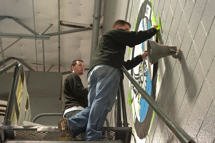 Staff Sgt. Daniel Sullivan, 823rd Maintenance Squadron aircraft structural maintenance craftsman, and Michael Sullivan, artist and brother of Sergeant Daniel Sullivan, peel tape off of the new 823rd MXS unit patch Dec. 15, 2012, at Nellis Air Force Base, Nev. The squadron changed its name to match its sister-squadrons, the 723rd MXS of Moody AFB, GA., and the 923rd MXS of Davis-Monthan AFB, Az. (U.S. Air Force photo by Staff Sgt. Christopher Hubenthal)