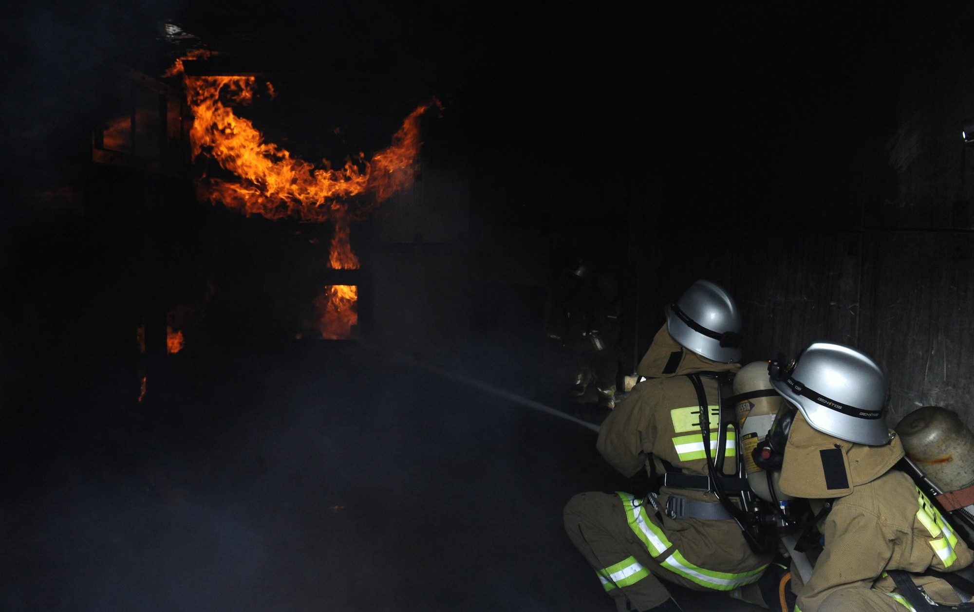 Firefighters extinguish a fire during a mutual aid live fire training on Kadena Air Base, Japan, Dec. 17, 2012. Nirai and Okinawa City firefighters trained on simulated interior fire scenarios where they had to put out flames in a kitchen and navigate through a building looking for victims and clearing smoke. The training also brought together the two different training styles to prepare them for real world joint fire fighting with Kadena firefighters. (U.S. Air Force photo/Airman 1st Class Malia Jenkins)   