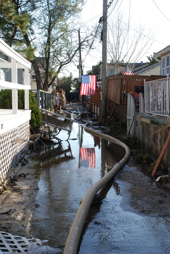 An American flag is reflected in a sand- and debris-filled alley in Breezy Point, N.Y., Nov. 9, where service members operating under the U.S. Army Corps of Engineers through a FEMA mission assignment cleared debris, conducted assessments, and pumped water from critical facilities and public housing areas in devastated beachfront communities. The joint task force used more than 70 pumps in 15 public housing complexes and one waste water treatment plant. In Breezy Point, Queens, they pumped an average of 750,000 to 1 million gallons of water per day. 