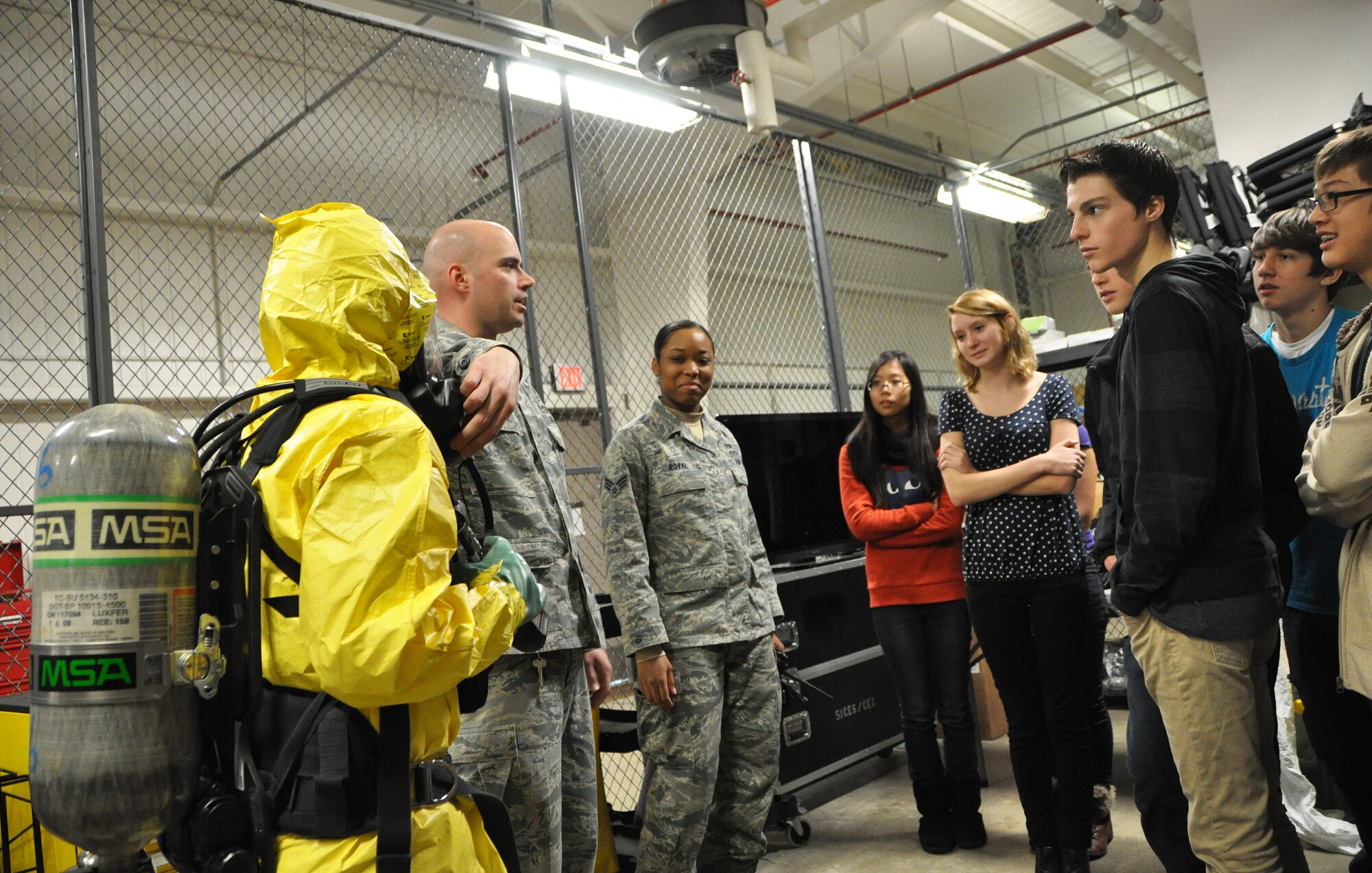Airman 1st Class Lisa Sandah (far left), 51st Civil Engineer Squadron emergency management journeyman, demonstrates the proper wear of a Level B suit, protective gear used for Chemical, Biological, Radiological, Nuclear or Explosive response, for the 10th grade Osan High School chemistry class that visited the emergency management flight Dec. 14, 2012.  Tech Sgt. Bradley Baker (left), 51st CES emergency management craftsman, and Senior Catrina Royal (right), 51st CES emergency management journeyman, assist.  (U.S. Air Force photo/Senior Airman Kristina Overton)