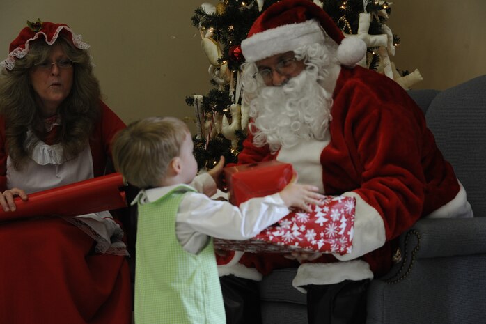 Two-year-old Joey Zujus, son of 1st Lt. Joseph Zujus, 14th Airlift Squadron, receives a present from Santa Clause while Mrs. Clause checks the naughty or nice list Dec. 15, 2012, during the third Annual Deployed Children’s Holiday Party hosted by the Team Charleston Honorary Commander’s Advisory Council at Joint Base Charleston – Air Base, S.C.  (U.S. Air Force photo/ Master Sgt. Maria Bare)