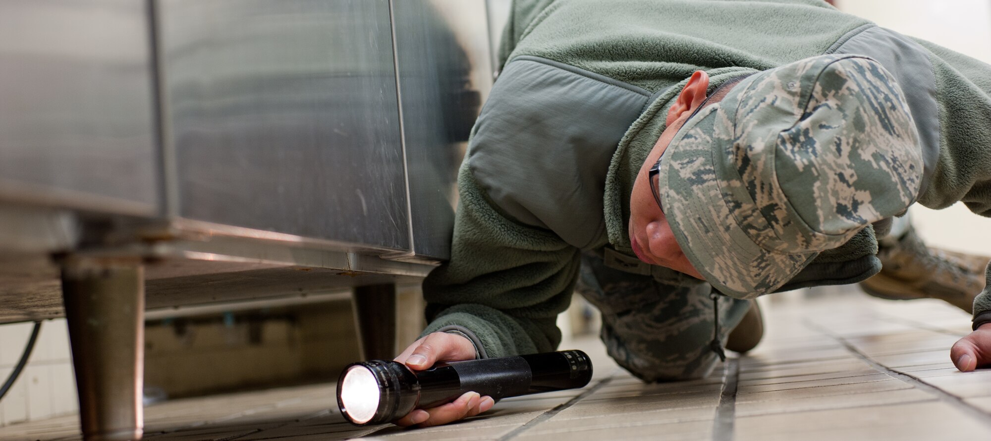 YOKOTA AIR BASE, Japan -- Senior Airman Perry Neang, 374th Civil Engineer Squadron Pest Management technician, inspects under equipment at the 374th Medical Group’s dining facility Dec. 19, 2012, at Yokota Air Base, Japan. During inspections, the pest management team looks for any recent insect activity and also set traps. (U.S. Air Force photo by Airman 1st Class John D. Partlow)