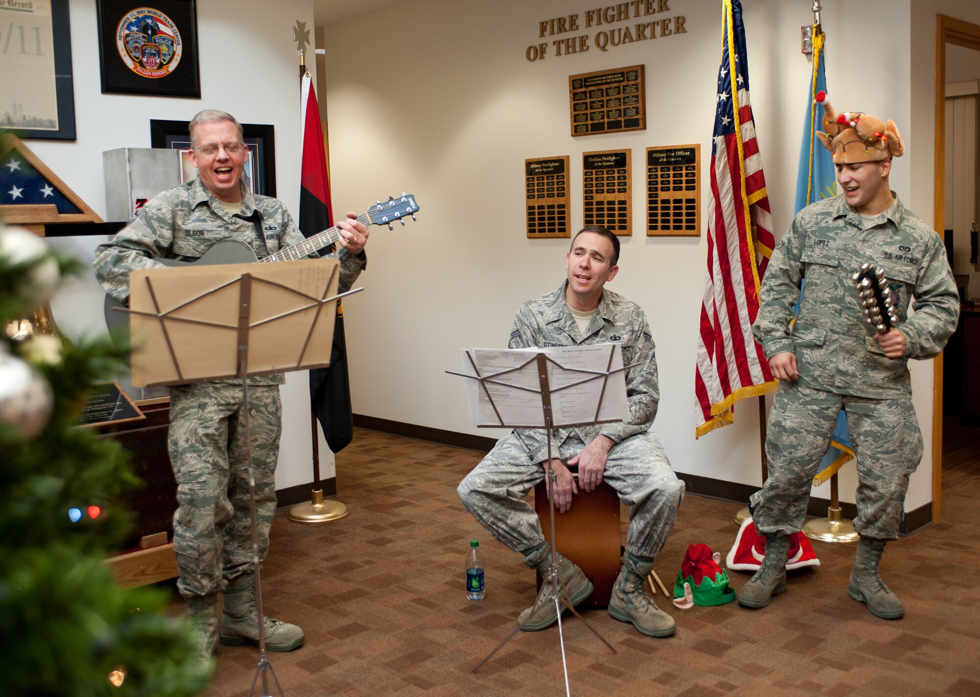 Airman Brandon Lopez (right), 28th Civil Engineer Squadron fire fighter, plays sleigh bells with Senior Airman Gary Steinberg (middle), USAF Heartland of America Band percussionist, and Master Sgt. Gary Olson, (left) NCO in charge and acoustic guitar player, during the performance of “Jingle Bells” at the Fire Department on Ellsworth Air Force Base, S.D., Dec. 18, 2012. Lopez was invited to play the sleigh bells with the band, as were many other Airmen during their performance. (U.S. Air Force photo by Airman 1st Class Alystria Maurer/Released)