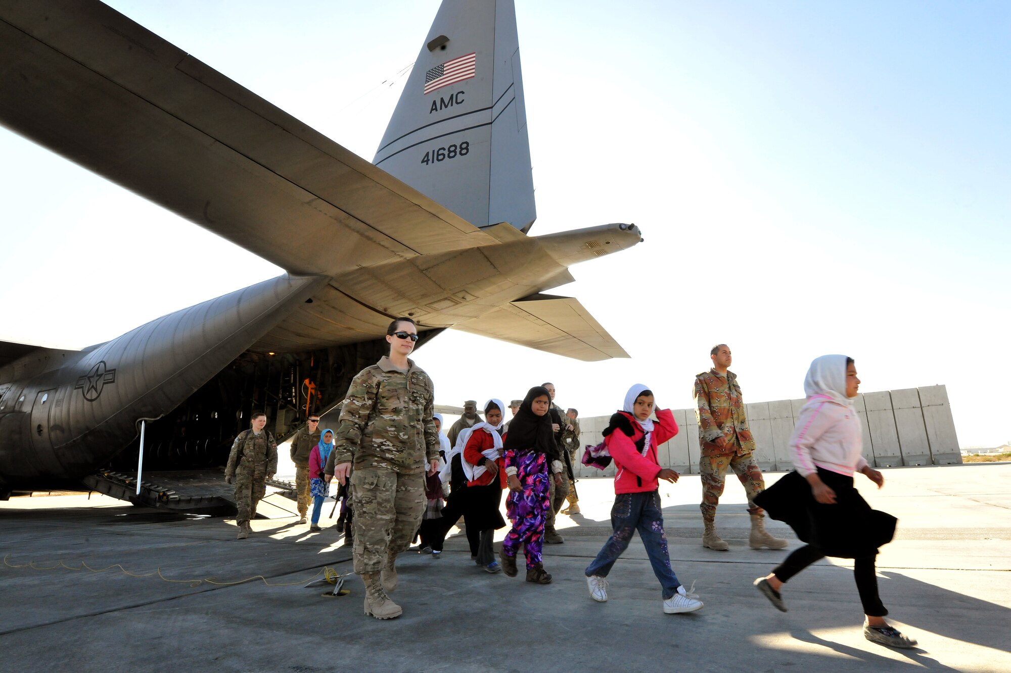 Military members and local Afghan girls enrolled in the “Cat in the Hat” education program depart a C-130 Hercules at Bagram Airfield, Afghanistan, Dec. 20, 2012. The educational outreach program supports the International Security Assistance Force’s counter-insurgency efforts by enabling positive interaction between U.S. servicemembers and the local community. (U.S. Air Force photo/Senior Airman Chris Willis)