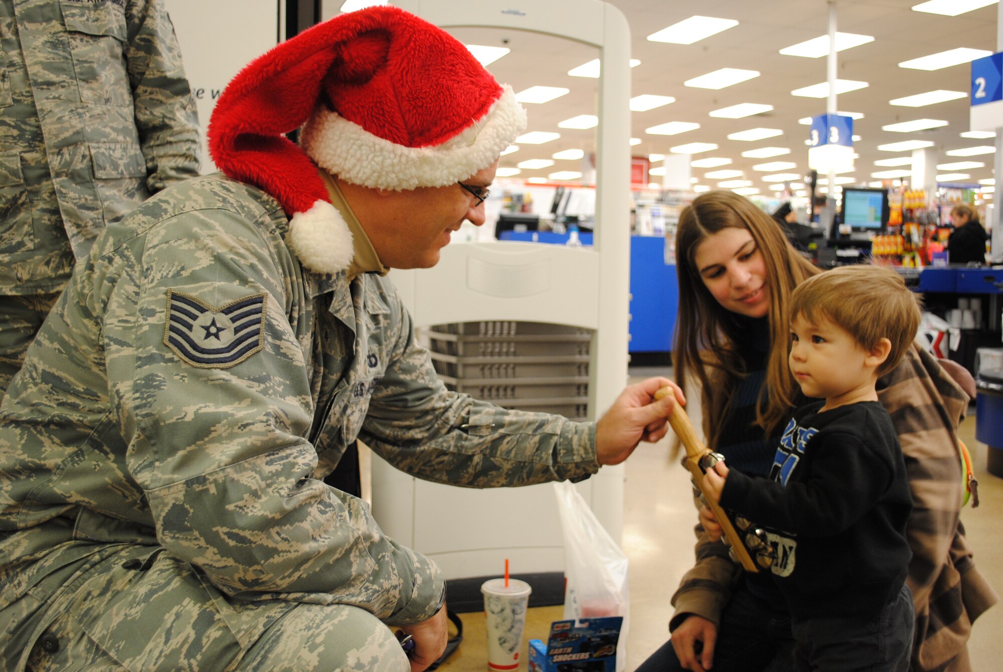 Tech. Sgt. James Mangette, offers a young patron the opportunity to play the sleigh bells during a short holiday-musical performance Dec. 18, 2012, at the Exchange on Grand Fork Air Force Base, N.D. Members of the United States Air Force Heartland of America Band toured the base for two consecutive days, performing holiday songs at 22 locations around the base. (U.S. Air Force photo/Senior Airman Luis Loza Gutierrez)