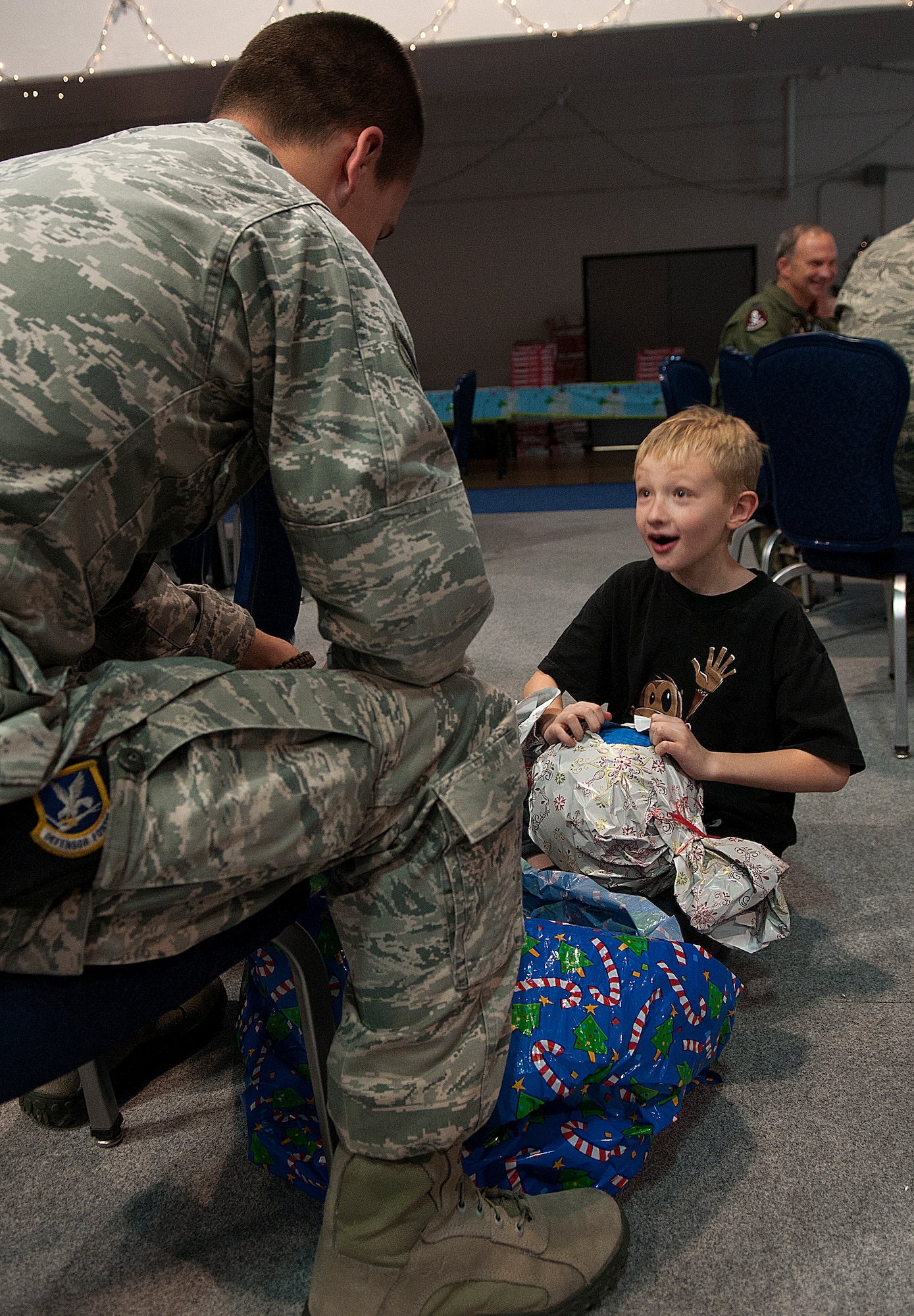 Braydon Nelson, 9, unwraps a present as his escort, Senior Airman Brandon Russell, 90th Missile Security Forces Squadron, looks on during Operation Provide Joy Dec. 15. (U.S. Air Force photo by R.J. Oriez)