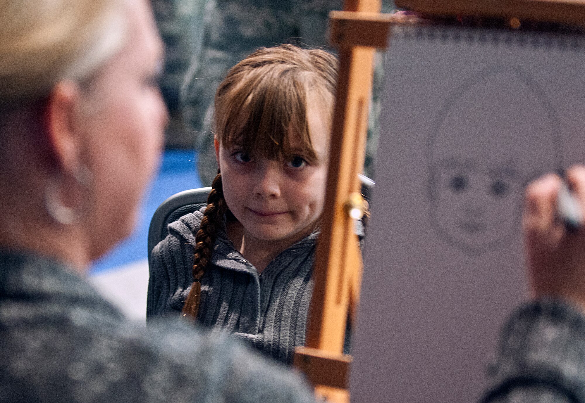 Alexis Hassler, 8, has a caricature of herself drawn by Melanie Kinney, a volunteer at Operation Provide Joy, in the Fall Hall Community Center Dec. 15. (U.S. Air Force photo by R.J. Oriez)