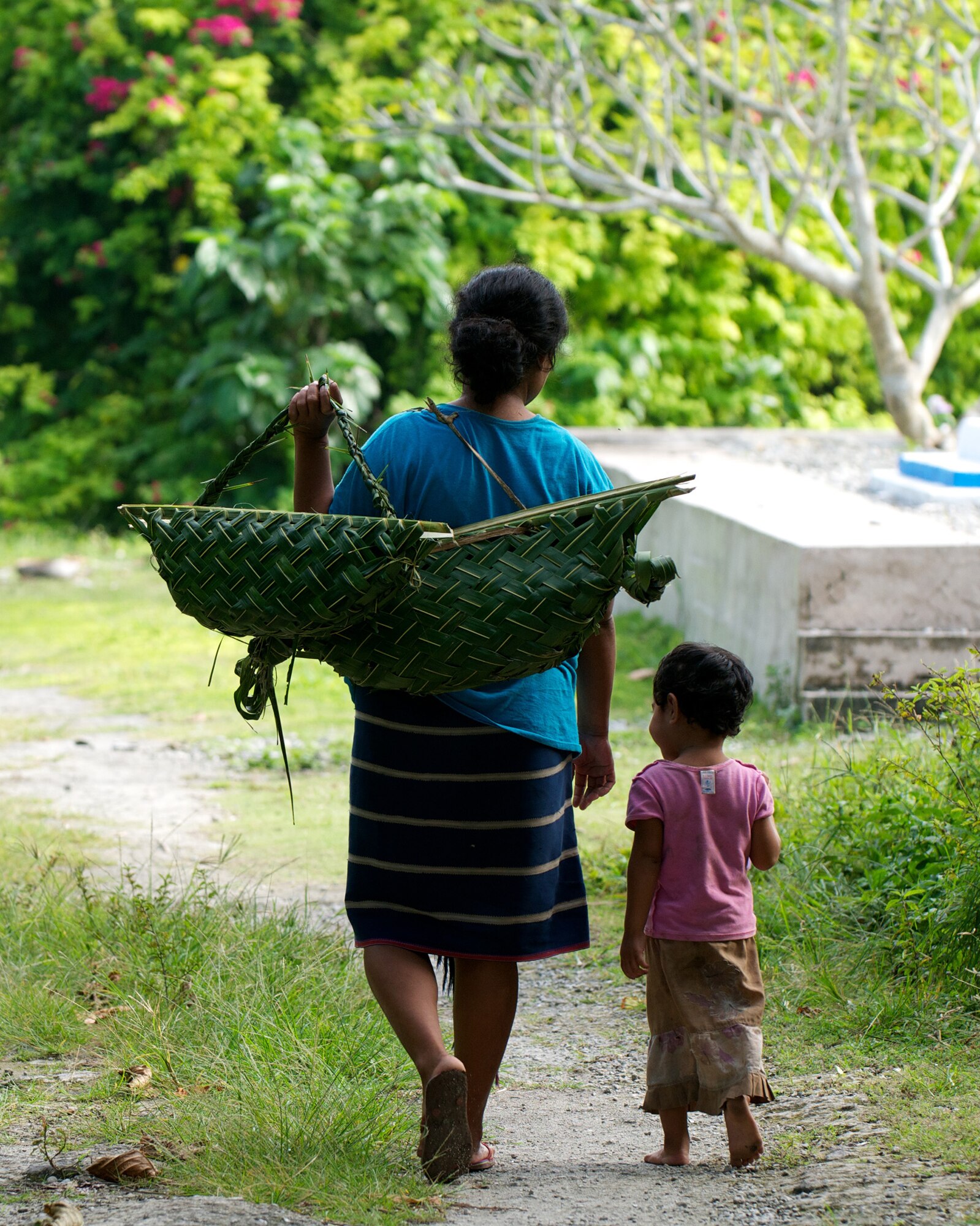 A woman and child walk down a path carrying handmade baskets on an island in Micronesia, Dec. 17, 2011. Master Sgt. Cameron Leslie visited the island to learn about the culture and how the islanders view Operation Christmas Drop. (Courtesy photo by Master Sgt. Cameron Leslie)