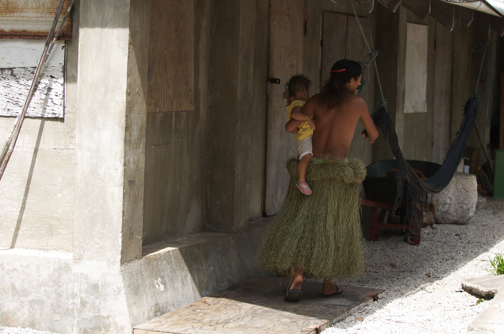 A woman walks away from the camera carrying her child and wearing a grass skirt on an island near Falalop, Micronesia, in 2011. The remote islands in Micronesia don't have established commerce in many cases, so many items taken for granted in western society are not available. (Courtesy photo by Master Sgt. Cameron Leslie)