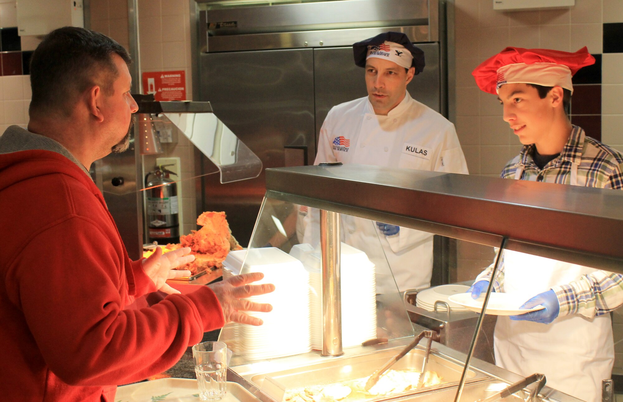 Col. Christopher Kulas, 100th Air Refueling Wing commander, and his son, Drew, serve William Johnson, Commissary employee, at the Gateway Dining Facility on Dec. 25, 2012, at RAF Mildenhall, England. The dining facility served a special holiday meal for all authorized patrons from 11 a.m. – 4 p.m. The meal included a shrimp cocktail appetizer, ham, turkey, roast beef and stuffing among a wide variety of other traditional dishes. Throughout the day, various commanders, chief master sergeants, first sergeants and other leaders from Team Mildenhall served the meal to dining facility customers. (U.S. Air Force photo by Capt. Jason Smith/Released)