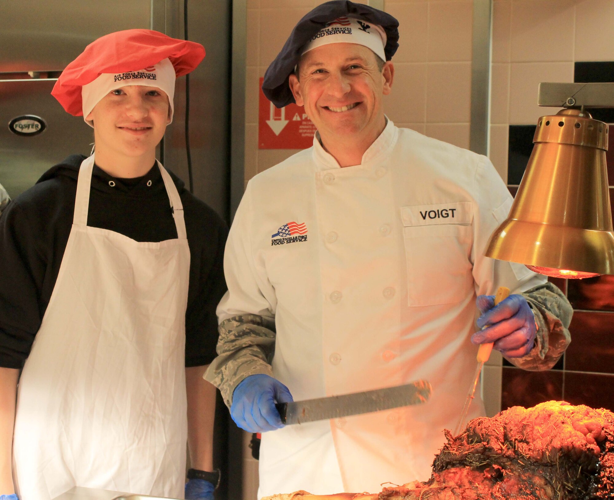 Col. Kyle Voigt, 100th Air Refueling Wing vice commander, and his son, Matthew, prepare to carve steamship round at the Gateway Dining Facility on Dec. 25, 2012, at RAF Mildenhall, England. The dining facility served a special holiday meal for all authorized patrons from 11 a.m. – 4 p.m. The meal included a shrimp cocktail appetizer, ham, turkey, roast beef and stuffing among a wide variety of other traditional dishes. Throughout the day, various commanders, chief master sergeants, first sergeants and other leaders from Team Mildenhall served the meal to dining facility customers. (U.S. Air Force photo by Capt. Jason Smith/Released)