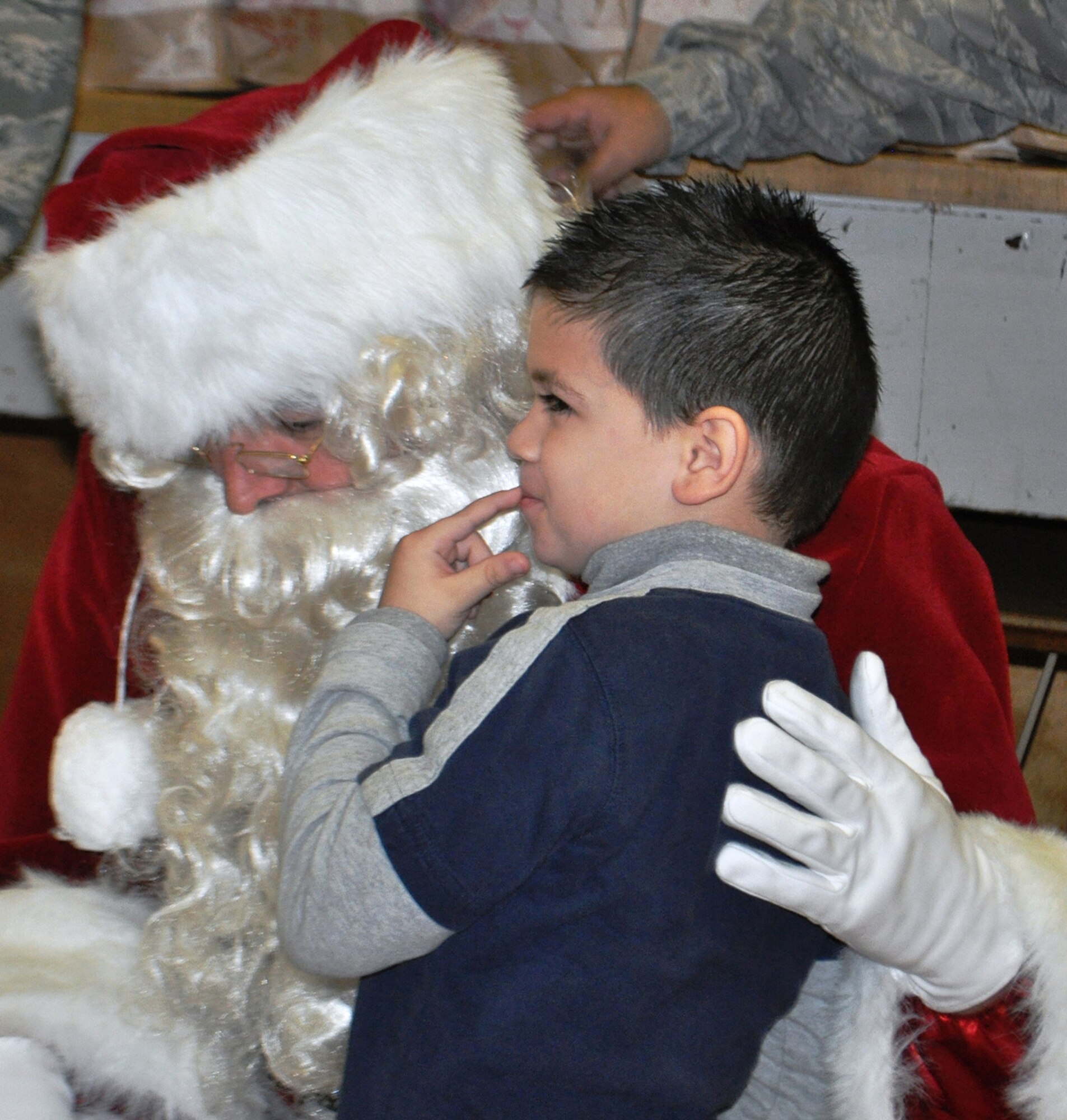 TRAVIS AIR FORCE BASE, Calif. -- "Santa," Chief Master Sgt. Mark Kloeppel, waits for a whispered request in his ear, as a kindergartener thinks about what he wants. Along with his Travis elves, the jolly old elf visited Cleo Gordon Elementary School as well as three others, to visit with kindergarten classes, and gift each child with a bag of goodies, small gifts, and of course, Teddy bears. The 349th AMW's Operation Teddy bear has been giving back to Solano community children for many years, giving them a more joyful holiday. (U.S. Air Force photo/Senior Master Sgt. Ellen Hatfield)