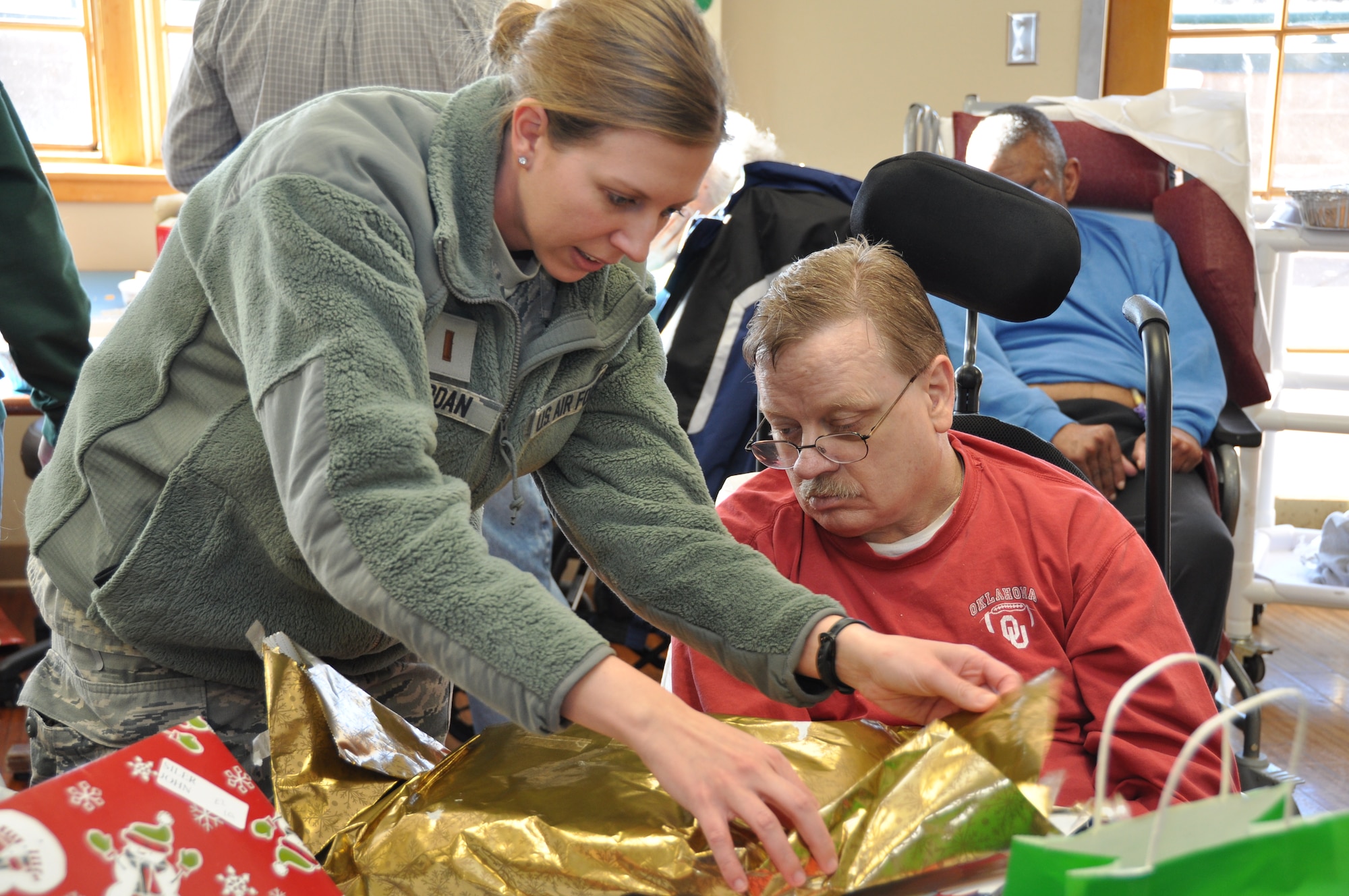 2nd Lt. Cristi Jordan, a 507th Operations Support Flight intelligence analyst helps Robert McCarthy, a veteran at the Norman Veterans Center, open a gift at the annual Christmas Party recently.  Over $4,000 was raised by members of the 507th Air Refueling Wing for gifts to be donated to the veterans.  Members of the 507th have been donating gifts since the center opened in 1996.  (Photo by Senior Airman Mark Hybers)