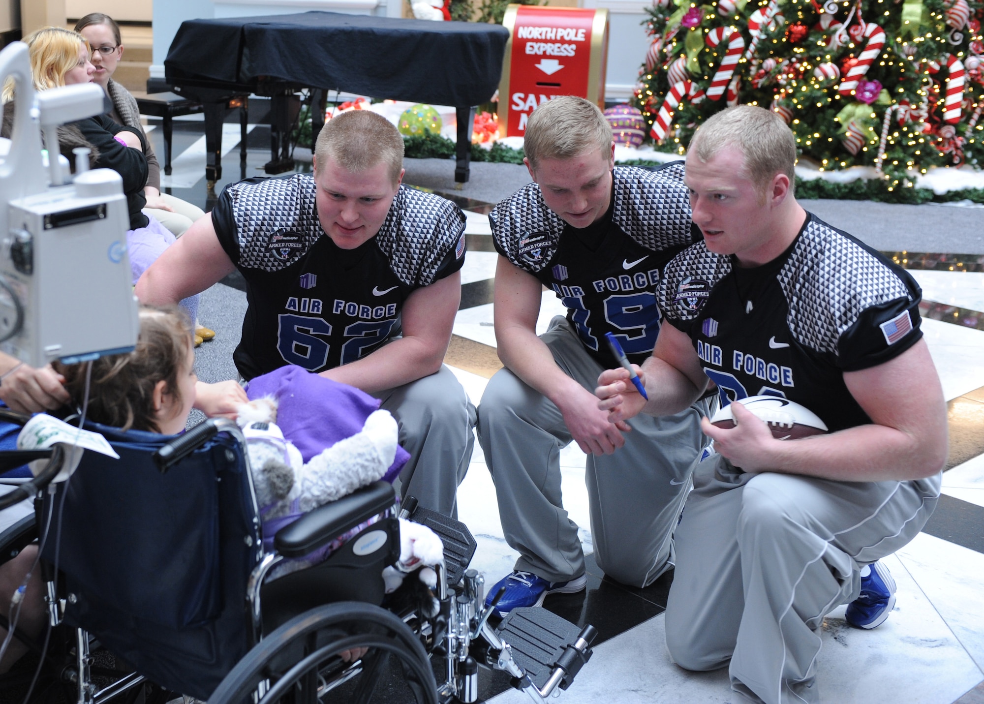 Air Force football players David Lore, Zach Hoffman and Troy Timmerman talk with and autograph a football for a patient at the Cooks Children's Medical Center in Fort Worth, Texas, Dec. 27, 2012. Lore is a starter at guard and a backup center; Hoffman is a punter, and Timmerman is a defensive lineman. (U.S. Air Force photo/John Van Winkle)