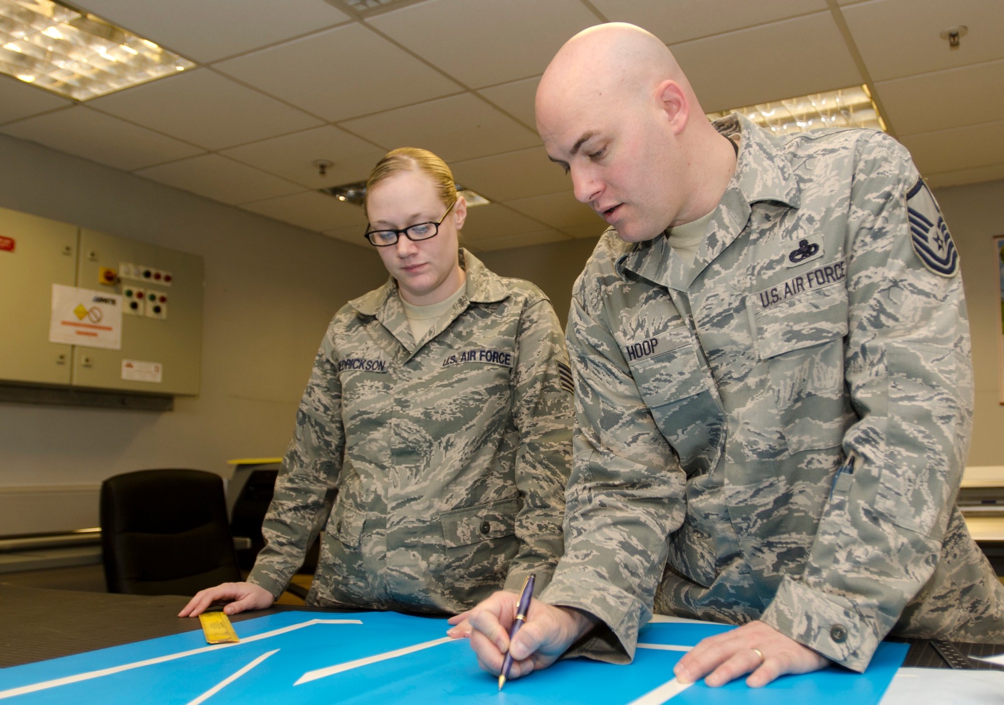 ROYAL AIR FORCE LAKENHEATH, England - Master Sgt. Ron Hoop (right), 48th Equipment Maintenance Squadron corrosion control NCO in charge, and native of Radcliffe, Ky., and Staff Sgt. Tabitha Fredrickson, 48th EMS aircraft structural craftsman and native of Pulaski, Wis., discuss aircraft marking layout Dec. 20, 2012. Each stencil is made for a specific aircraft, which it is applied to and painted over. (U.S. Air Force photo by Staff Sgt. Stephen Linch)