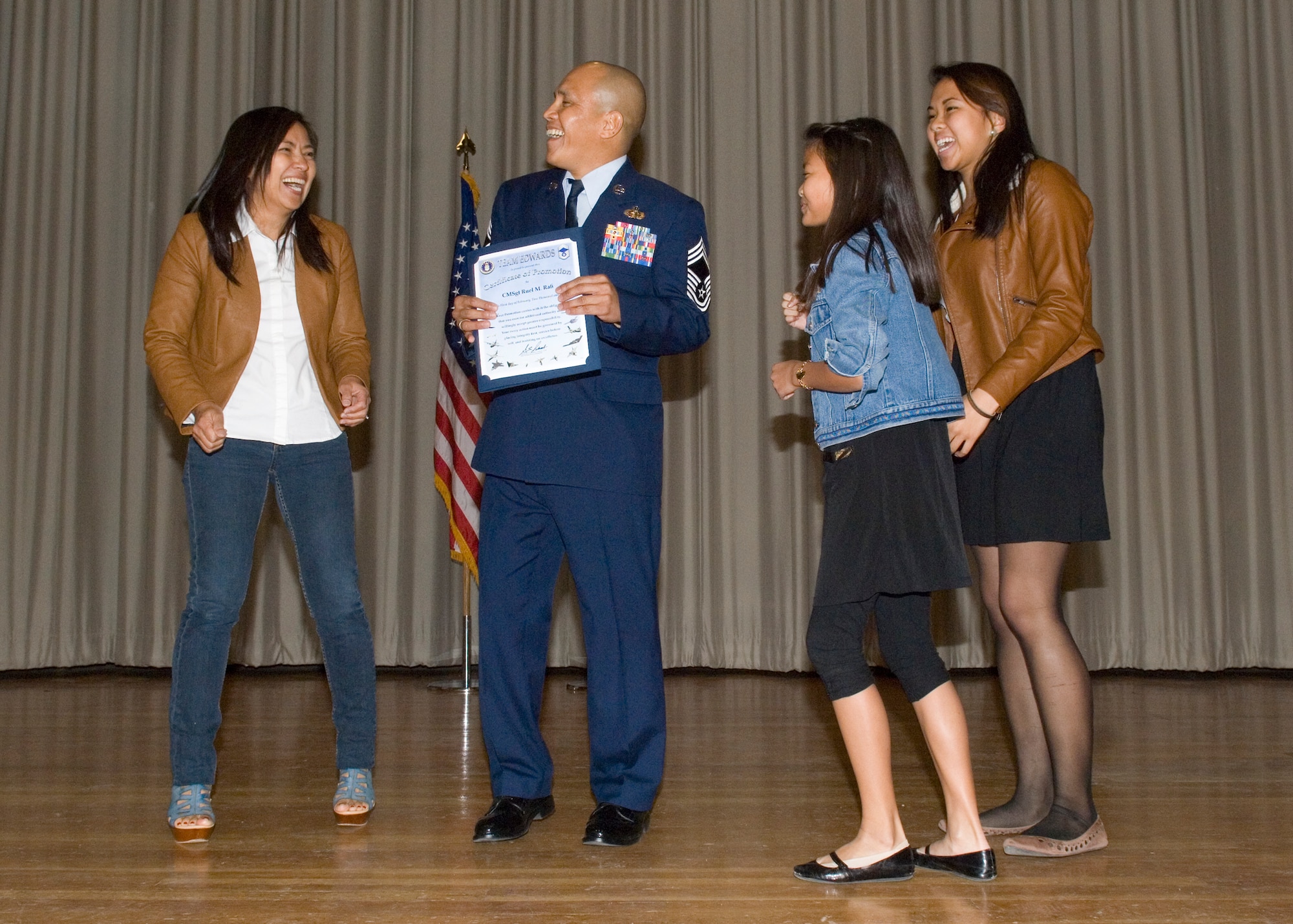 Newly promoted Chief Master Sgt. Ruel Rafi, 95th Communications Squadron, enjoys a moment on stage with his family during the January and February promotion ceremony Jan.31 in the Base Theater. (U.S. Air Force photo by Rob Densmore)