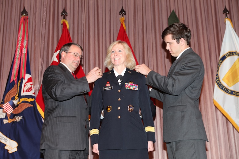 WASHINGTON — Brig. Gen. Margaret W. Burcham's husband, Jay Burcham, Chief of Staff of the Department of Defense Education Activity (left), and her son, John Tubesing, University of Virginia student, pinned on her new rank amidst applause from the audience. Brig. Gen. Burcham became the Army Corps of Engineers' first female general officer, during her promotion ceremony at the headquarters here, Jan. 27, 2012. Last September, Burcham became the first woman selected to command a Corps of Engineers division when she took command of the Great Lakes and Ohio River Division located in Cincinnati, OH. The division consists of seven engineer districts that include over 4800 personnel operating in a 17 state region with the responsibility for the federal water resource development throughout the Great Lakes and Ohio River basins.
