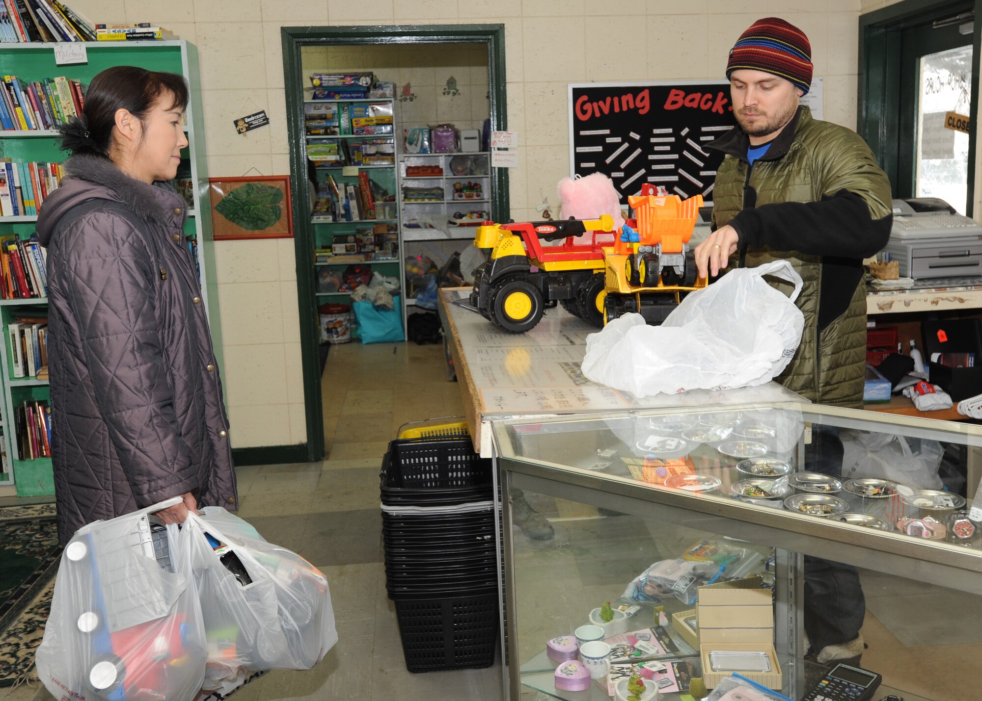 MISAWA AIR BASE, Japan – Josh Brown, Thrift Shop manager (right), checks out and bags toy trucks for a thrift shop customer here, Feb. 1. Brown has worked at the shop for 18 months, along with other paid employees and volunteers. (U.S. Air Force photo/Airman Kenna Jackson)