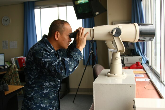 Petty Officer 2nd Class Bellan M. Rombawa, boatswain’s mate, peers out of a high powered telescope to over view the harbor near the airfield here Feb. 1. The Harbor must remain under constant supervision to ensure no one gets near the air station who does not belong. Harbor operations also keeps the station’s coast secure against any threats. Without Harbor Operations many exercises and consistent training would come to a halt.