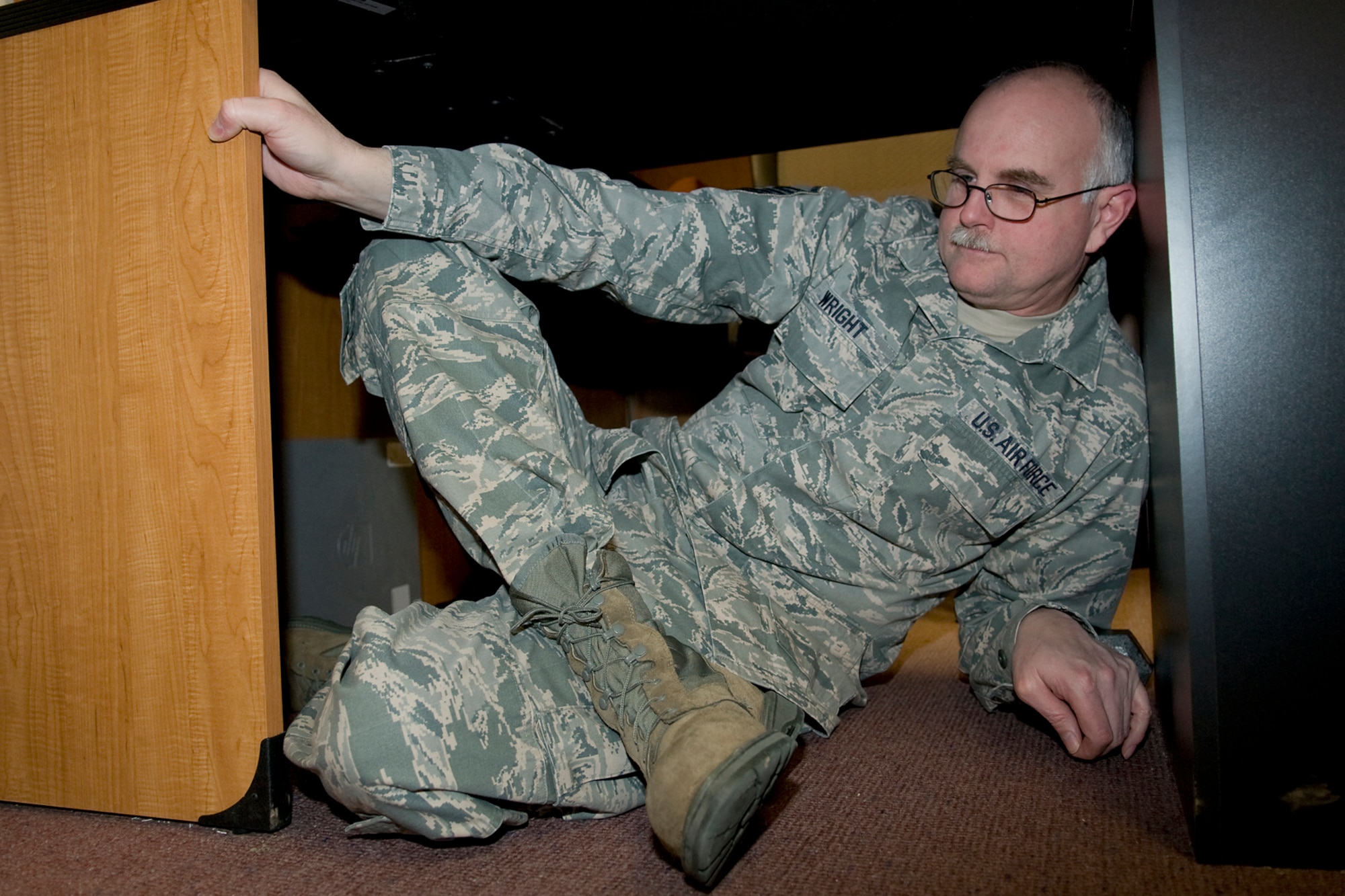 GRISSOM AIR RESERVE BASE, Ind. -- Master Sgt. Ronald Wright, 434th Air Refueling Wing career advisor, positions himself under a desk here as he takes part in an earthquake drill Feb. 7. Grissom personnel dropped, covered and held on during a Great Central U.S. ShakeOut earthquake drill along with millions of other Americans. (U.S. Air Force photo/Tech. Sgt. Mark R. W. Orders-Woempner)

