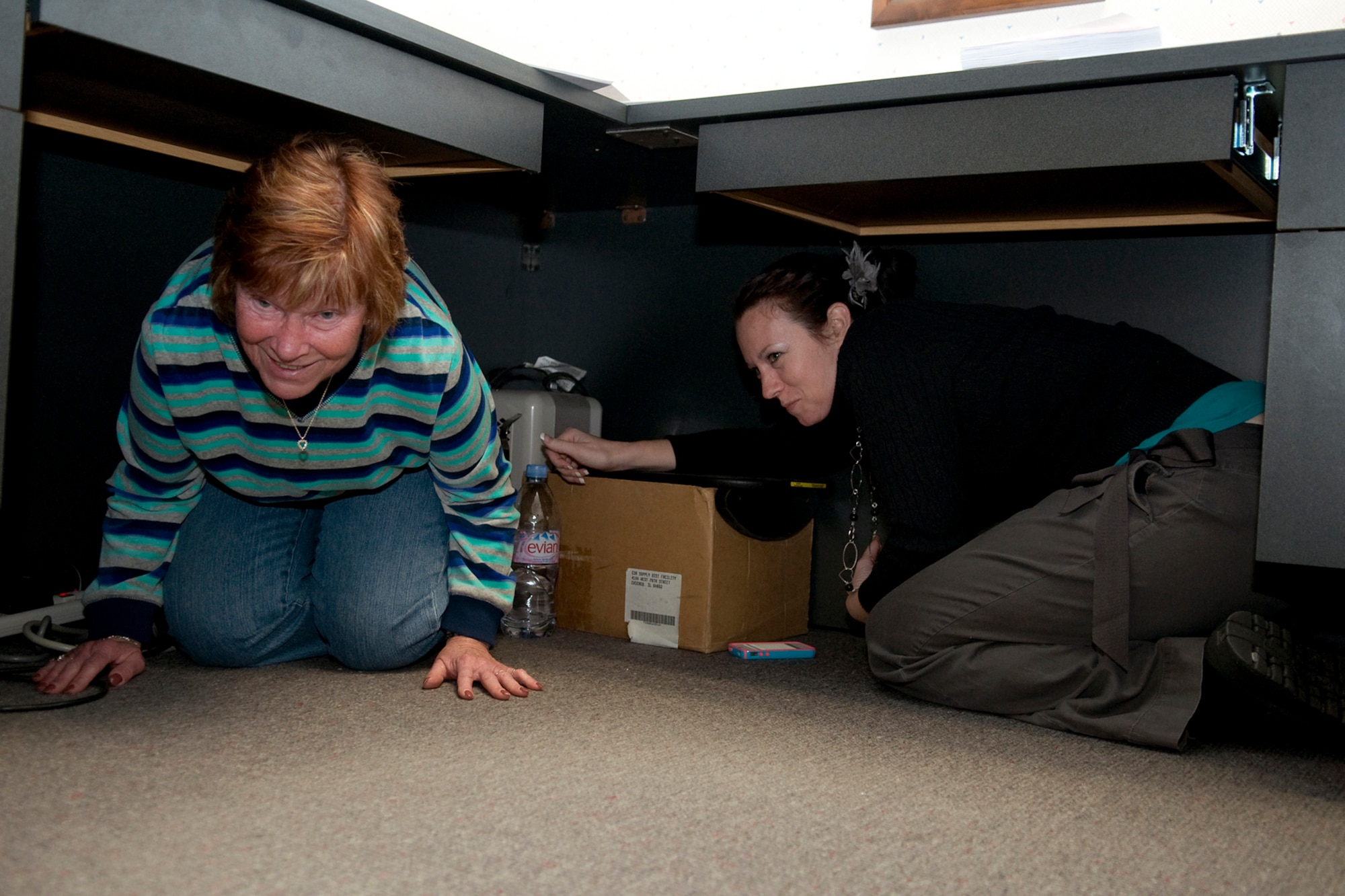 GRISSOM AIR RESERVE BASE, Ind. -- Judi Behny, left, and Rachelle Hill-Wells take cover under a desk during a simulated earthquake here Feb. 7. Grissom personnel participated in a Great Central U.S. ShakeOut earthquake drill along with millions of other Americans. Behny is a comptroller quality assurance manager and Hill-Wells is a budget operations and management analyst. Both are assigned to the 434th Air Refueling Wing. (U.S. Air Force photo/Tech. Sgt. Mark R. W. Orders-Woempner)
