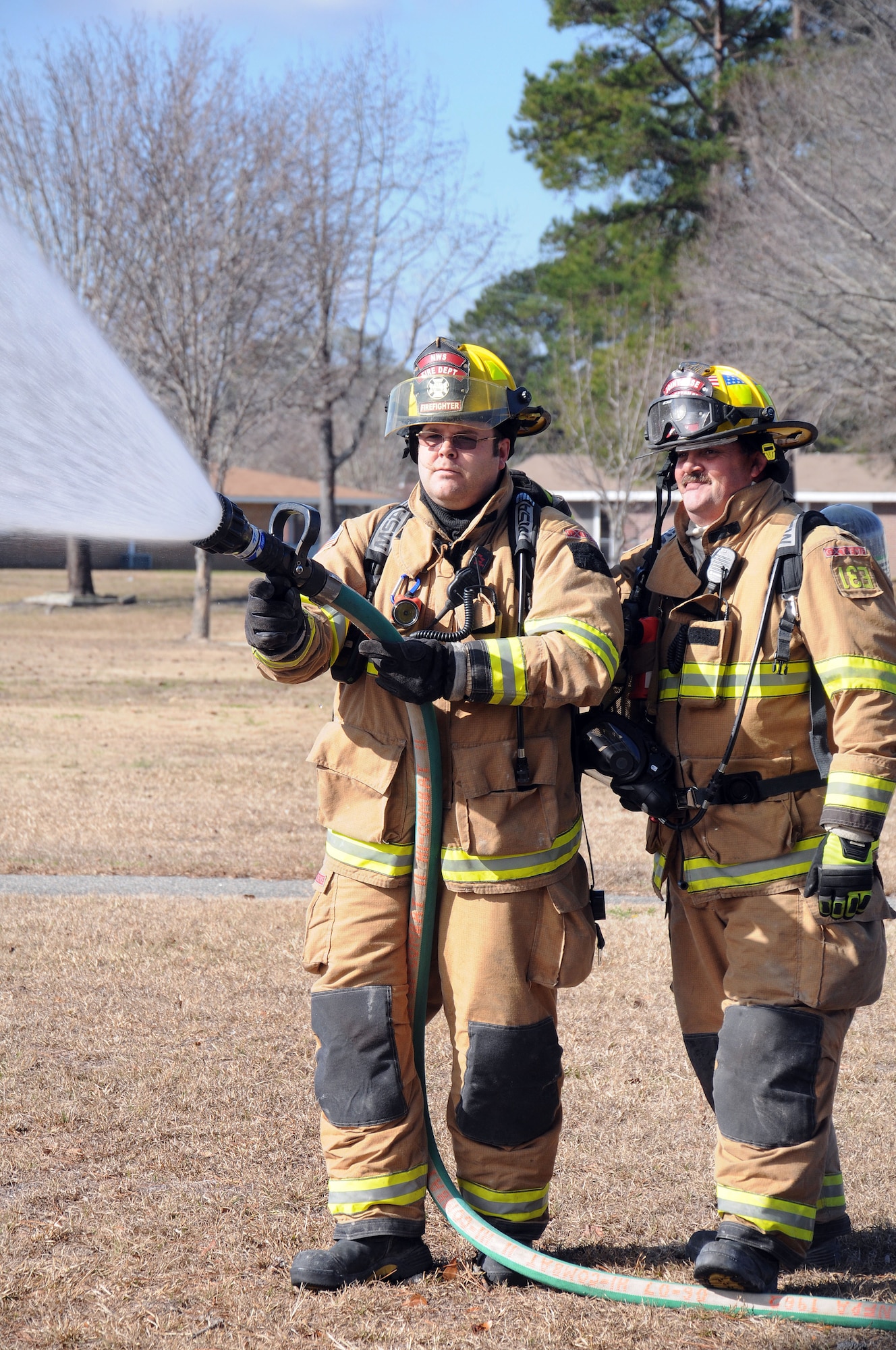 Firefighter Dominic Rend mans the nozzle as Firefighter Michael Brady holds down the hose with his foot and supports his partner as they simulate extinguishing a fire during an exercise at Joint Base Charleston – Weapons Station Feb. 2. The exercise was held to test the unit’s response to a simulated fire at a home in the Menriv Housing area. Rend and Brady are both assigned to the 628th Civil Engineer Squadron, Civil Engineer Fire Department. (U.S. Navy photo/Petty Officer 1st Class Jennifer Hudson)