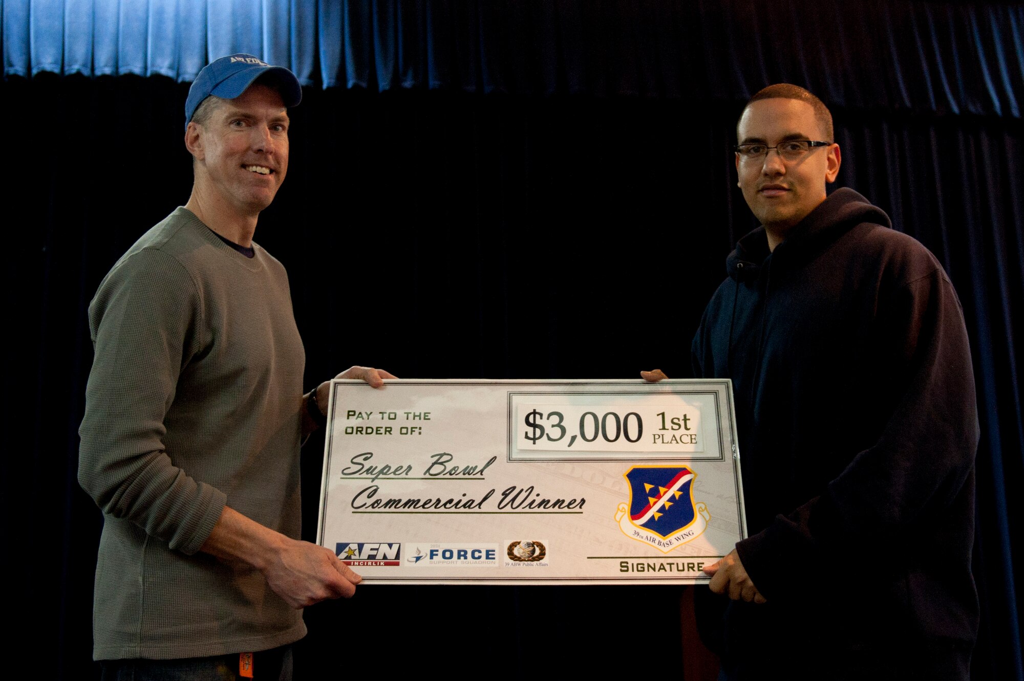 Senior Airman Robert Steinbacher, 39th Force Support Squadron, accepts a $3,000 check in wing funds on behalf of the 39th FSS from Col. Chris Craige, 39th Air Base Wing commander, after winning the Super Bowl XLVI commercial contest Feb. 6, 2012, at the Club Complex ballroom at Incirlik Air Base, Turkey. The 39th FSS won first and third place, winning $3,000 and $1,000, respectively; the 39th Maintenance Squadron won second, winning $2,000; and the individual category submission was from Nathan Kaw-Uh, who won a $100 voucher toward an Outdoor Recreation Connection trip. (U.S. Air Force photo by Tech. Sgt. Michael B. Keller/Released)