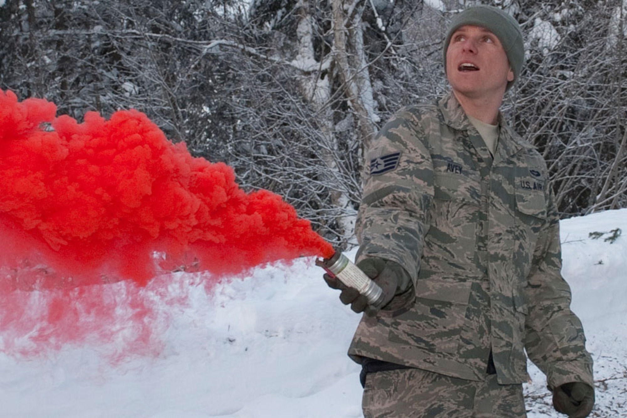Air Force Staff Sgt. Greg Avey sets off  a red-smoke signal after starting a fire using snow-covered branches and twigs from the surrounding trees during his Survive and Evade class on Joint Base Elmendorf Richardson Jan. 26. (U.S. Air Force photo/Staff Sgt. Robert Barnett)