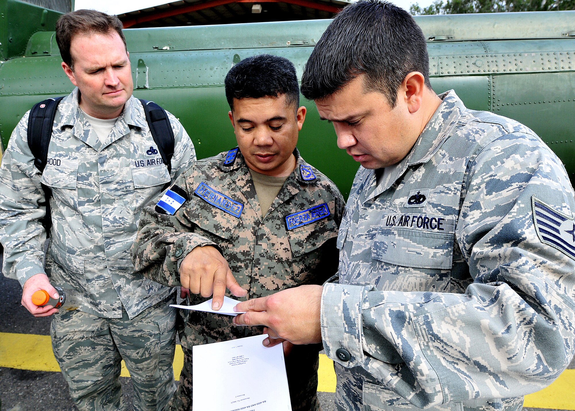Senior Master Sgt. Jason Hood, 571st Mobility Support Advisory Squadron helicopter crew chief and air advisor, listens in as Honduran Air Force Sub-official Master 2nd Class Enrique Hernandez Sanchez, FAH inspector, and Technical Sgt. Ruben Sigala, Inter-American Air Forces Academy instructor, discusses the inflight operational check of the radar altimeter system at Col. Hernán Acosta Mejia Air Base, Tegucigalpa, Honduras, Feb. 6.  (U.S. Photo by Tech. Sgt. Lesley Waters)