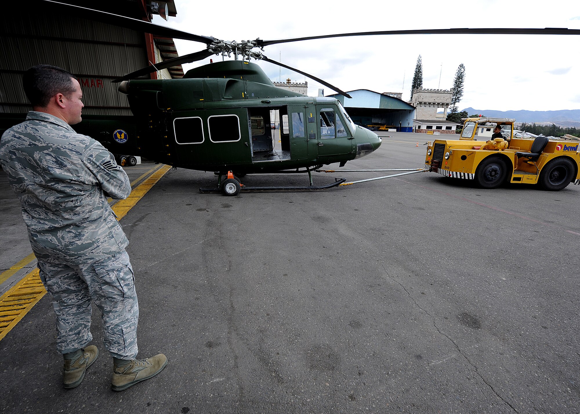 Staff Sgt. Heric Llerena, Inter-American Air Forces Academy instructor, 318th Training Squadron, Lackland AFB, Texas, looks on as members of the Honduran Air Force tows the helicopter with the newly installed radar altimeter system out of the hangar for the system's initial ground operational check, at Col. Hernán Acosta Mejia Air Base, Tegucigalpa, Honduras, Feb. 6.  (U.S. Photo by Tech. Sgt. Lesley Waters)