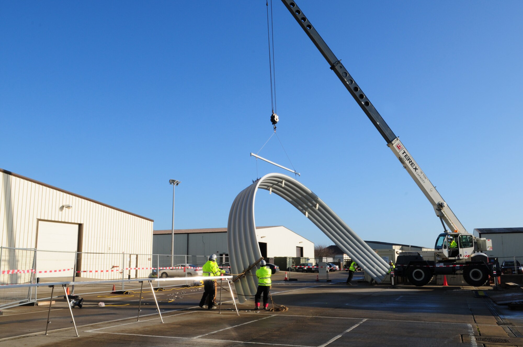 RAF MILDENHALL, England -- A pick (five steel panels joined together) is attached to a spreader bar and raised by a crane, before being moved and positioned into place as part of the K-Span structure on the south side of base Jan. 27, 2012. A team of 15 members from the 435th Construction and Training Squadron Military Construction Flight – 14 U.S. Air Force active duty and one German national – were here for one month building a K-Span facility (a half-moon-shaped building, made completely of steel).  (U.S. Air Force photo/Karen Abeyasekere)
