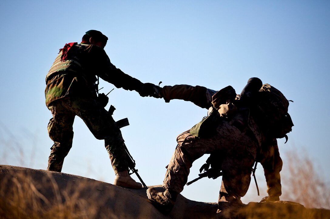 A noncommissioned Afghan army officer helps U.S. Marine Staff Sgt. Joshua Holden climb onto a roof while searching compounds during a security patrol in the Garmsir district in Afghanistan's Helmand province, Feb. 6, 2012. Holden is a section leader assigned to Weapons Company, 3rd Battalion, 3rd Marine Regiment. Marines from his unit and Afghan soldiers partnered to conduct census operations, and search houses for illegal drugs and evidence of insurgent activity.