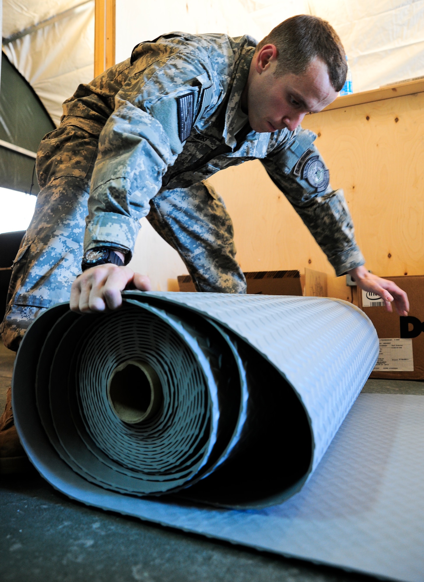 Aviation Ordnanceman 2nd Class John Ross rolls out floor covers Jan. 25, 2012, at the Naval Forces Central Command Forward Headquarters Manas at the Transit Center at Manas, Kyrgyzstan. Ross is one of the Sailors standing the NAVCENT FWD HQ Manas which will be responsible for moving and tracking Sailors into and out of Afghanistan. He is a liaison officer deployed here from the Naval Operations Support Center in Long Island, N.Y.(U.S. Air Force Photo/Staff Sgt. Angela Ruiz)