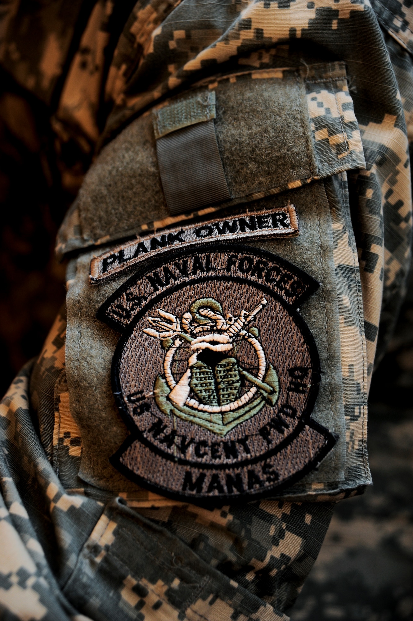 A proudly worn "Plank Owner" patch sits above the "U.S. Naval Forces Central Command Forward Headquarters Manas" patch Jan. 24, 2012, on a Sailor at the Transit Center at Manas, Kyrgyzstan. A plank owner is a member of the ship's crew when the vessel is  placed in commission. Today a plank owner is often applied to members of newly commissioned units, new military bases and recommissioning crews.(U.S. Air Force Photo/Staff Sgt. Angela Ruiz)
