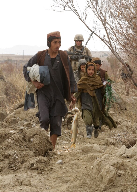 Local children with a fresh catch of fish walk past Lance Cpl. William M. Baldridge, a radio operator with, India Company, 3rd Battalion, 7th Marine Regiment, during a security patrol here recently. Baldridge, a 22-year-old native of Palmdale, Calif., spoke to the children in Pashto, the primary language here. During the past two years, Afghan National Army soldiers and Marines cleared the area of insurgents and developed positive relations with local villagers.