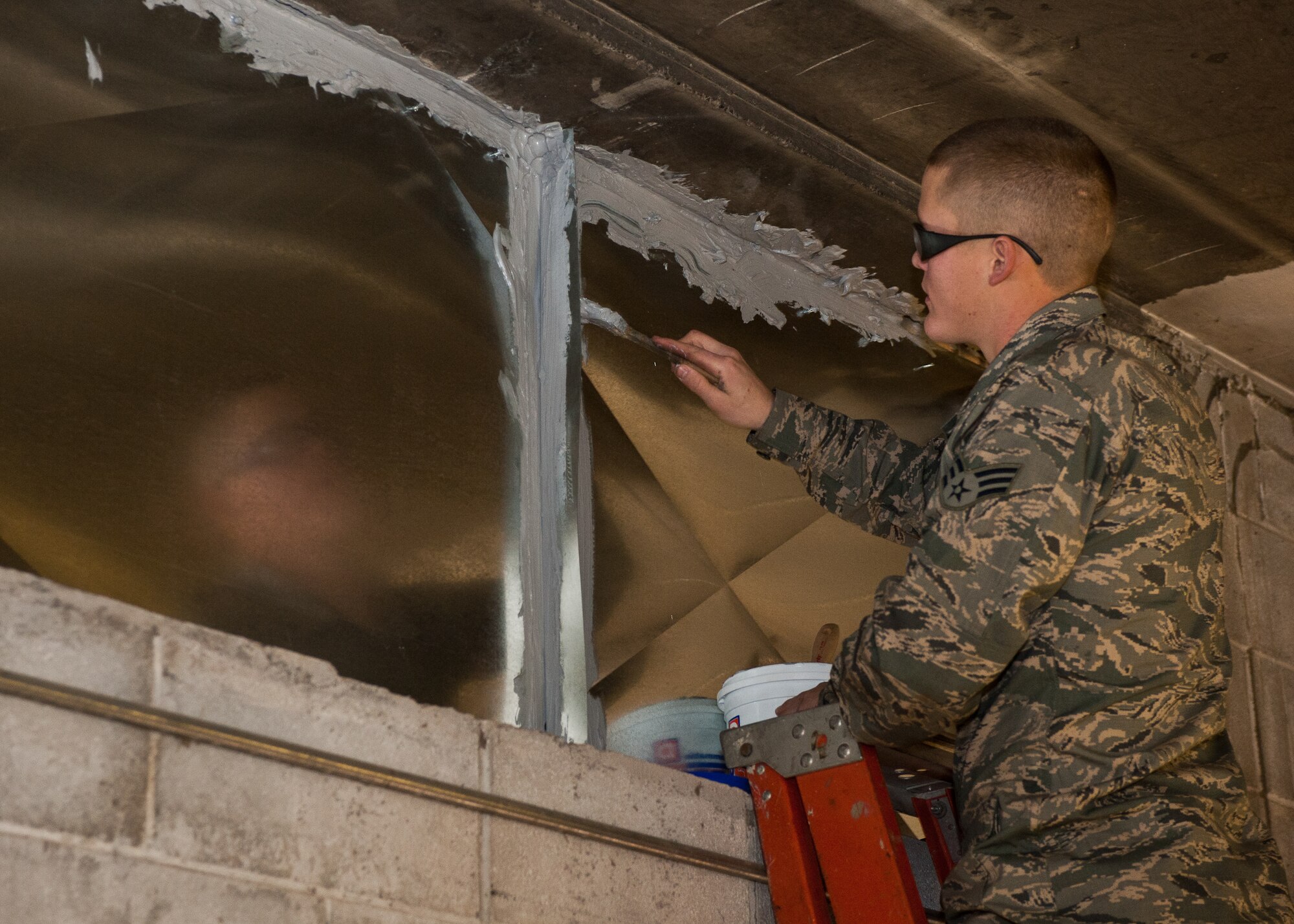 Senior Airman David McMillen, 28th Civil Engineer Squadron heating and air conditioning technician, applies caulk paste to sheet metal to create a seal on the side of dock 21 at Ellsworth Air Force Base, S.D., Feb. 2, 2012. By properly installing the system, technicians ensure efficient use and conservation of valuable resources in the facility. (U.S. Air Force photo by Airman Alystria Maurer/Released)