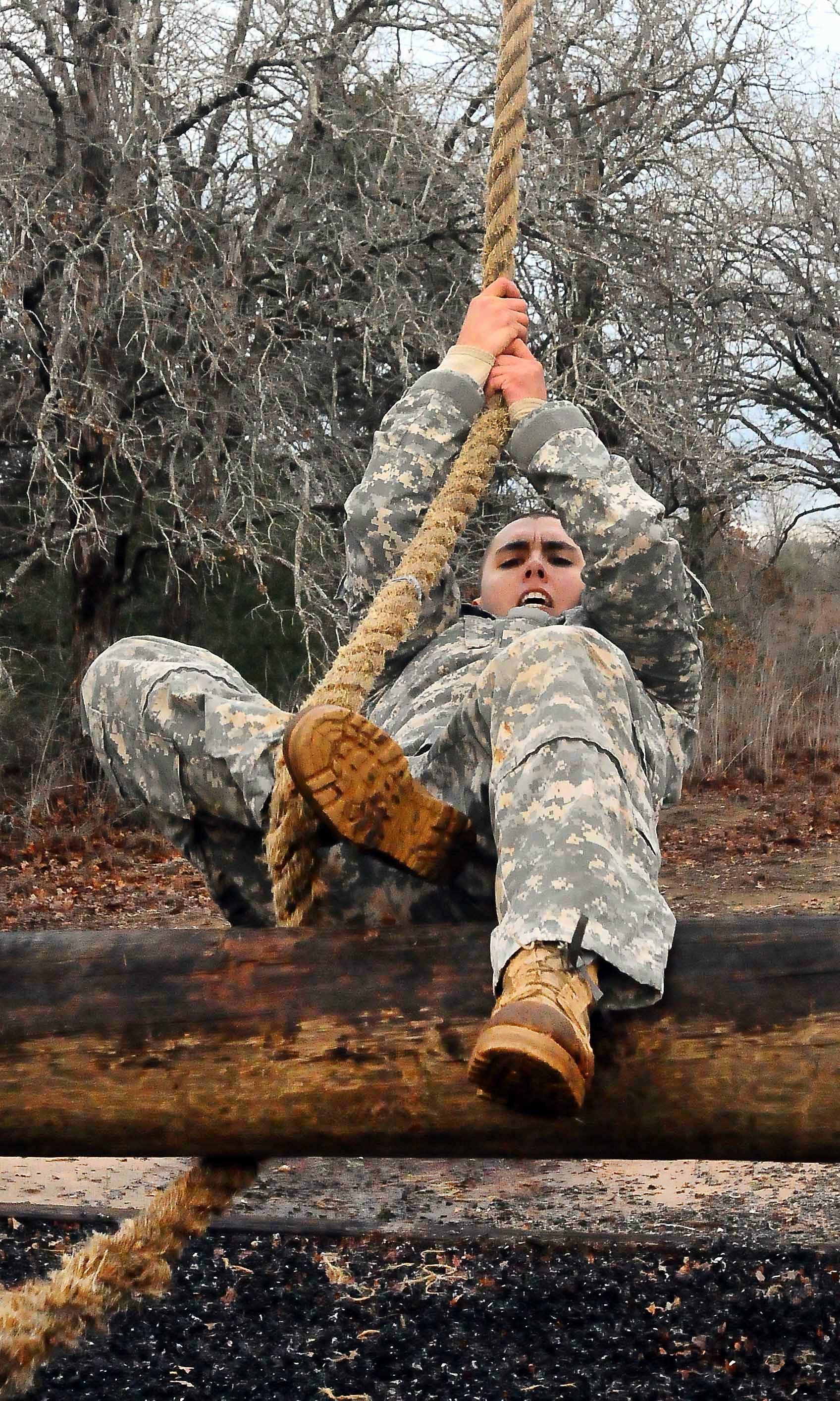 An Army National Guard soldier swings on a rope over a log obstacle