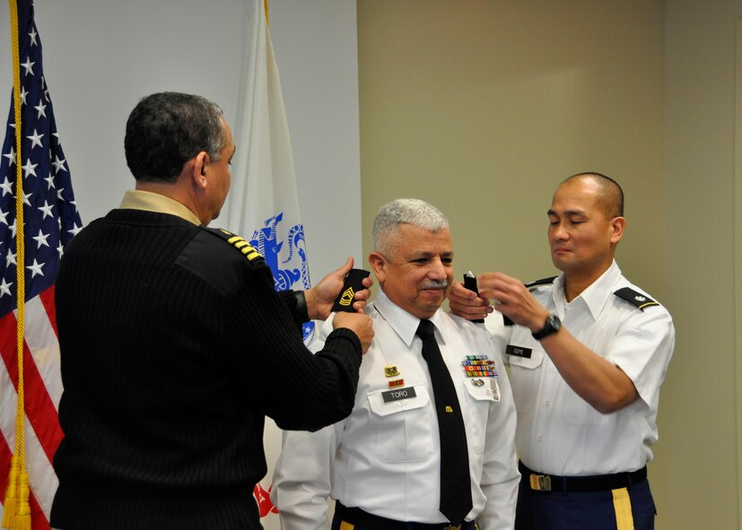 Navy Capt. Stephen L. Robinson, (left) Assistant Armed Forces Medical Examiner, and Army Lt. Col. Michael Cepe, (right) Army Liaison Team officer in charge at the port mortuary, place master sergeant rank on the epaulets of Army Sergeant 1st Class Jimmy Toro during a promotion ceremony Feb. 13, 2012, at the Armed Forces Medical Examiner’s Office, Dover Air Force Base, Del. Toro was recently reassigned to support the AFMES mission after serving for more than four years with the Army Liaison Team at the Charles C. Carson Center for Mortuary Affairs, under Casualty and Mortuary Affairs Operations Center, U.S. Army Human Resources Command, located at Fort Knox, Ky. Toro is part of the U.S. Army Reserve, 311th Quartermaster Company in Puerto Rico. (U.S. Air Force photo/Christin Michaud)