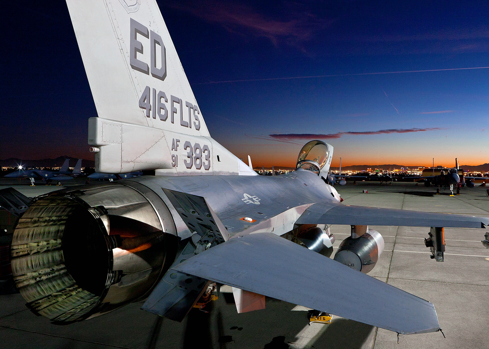 With the night lights of downtown Las Vegas and F-15s from the Republic of Korea Air Force serving as a backdrop, an F-16 from the 416th Flight Test Squadron awaits for its aircrew to prep the aircraft for a night sortie during Red Flag Jan. 25. (Lockheed Martin photo by Chad Bellay)