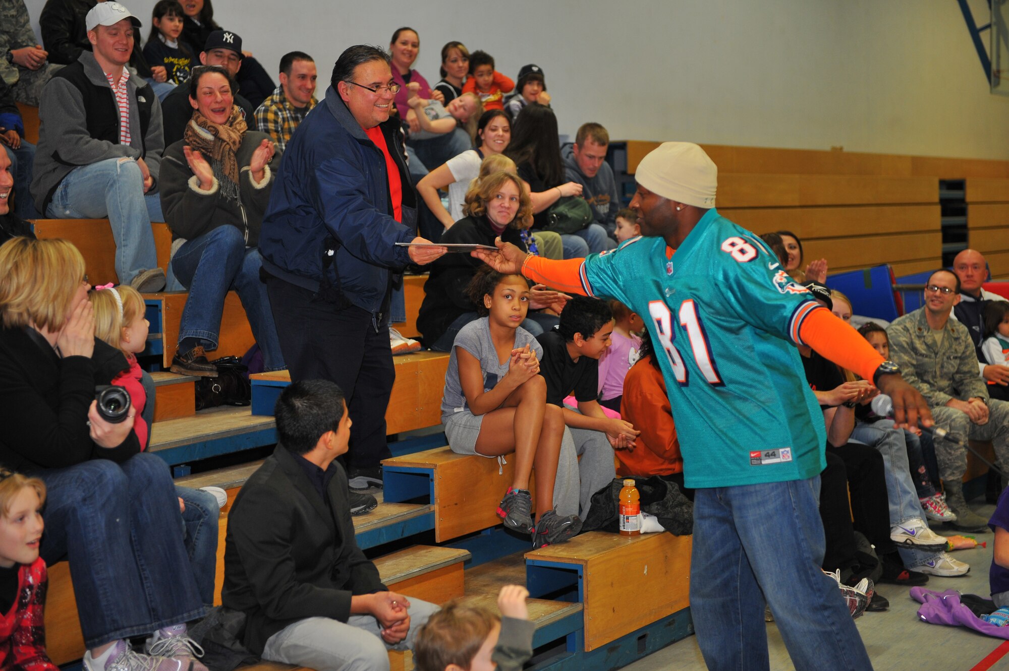SPANGDAHLEM AIR BASE, Germany – O.J. McDuffie, retired Miami Dolphins wide receiver, hands a sports calendar to a member of the audience during a team history trivia game at the Spangdahlem Middle School here Feb. 10. The Miami Dolphins football players and cheerleaders toured various U.S. Air Force and Army bases in Europe as part of an Armed Forces Entertainment tour. The reason for the visit was to boost morale and entertain the base’s community. (U.S. Air Force photo by Airman 1st Dillon Davis/Released)