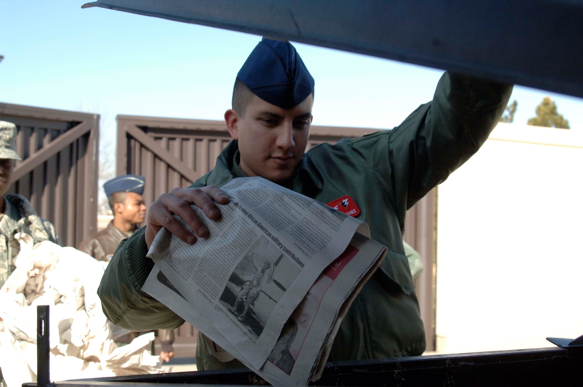Senior Airman Andre Sanchez, 3rd Space Operations Squadron, tosses old newspapers into a recycling dumpster outside the 50th Space Wing headquarters building here Feb. 15. Recycling dumpsters on base can now accept glass and plastic foam and all types of plastic. (U.S. Air Force photo\Scott Prater)