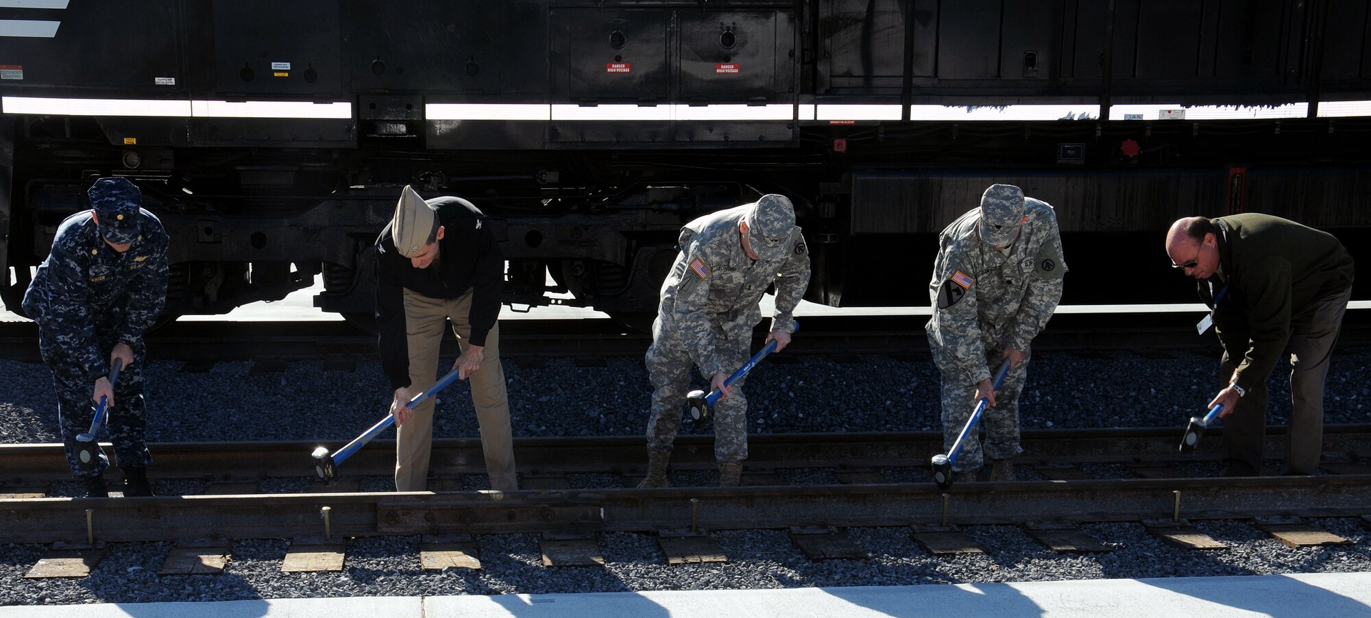 (Left to right) Lt. Cmdr. Stephen Fichter, Navy Capt. Ralph Ward, Army Maj. Gen. Kevin Leonard, Army Lt. Col. Robert Dawson and Terry Healey drive golden spikes during the 841st Transportation Battalion ribbon cutting and golden spike ceremony at Joint Base Charleston - Weapons Station Feb. 13. The golden spike ceremony represents the completion of an eight-year, $9 million project that expanded the rail facility to eight lines. Fichter is the Naval Facilities Engineering Command resident officer in charge of construction, Ward is the JB Charleston deputy commander, Leonard is the Surface Deployment and Distribution Command commanding general, Dawson is the 841st Transportation Battalion commander and Healey is the Queen City Railroad Construction site safety health officer.  (U.S. Navy photo/Petty Officer 2nd Class Brannon Deugan)