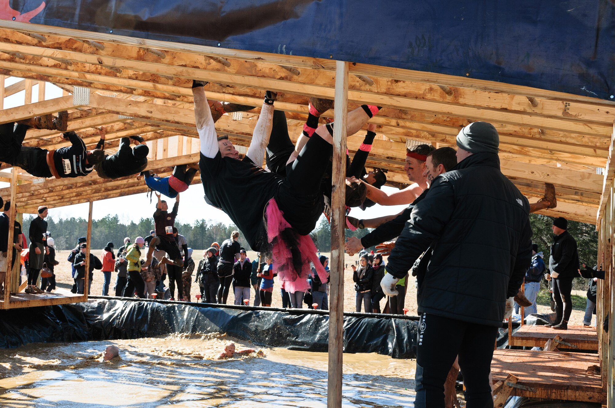 Staff Sgt. Jonathan Galvin (wearing pink), an Air Force Reserve line recruiter with Headquarters Air Force Reserve Command Recruiting Squadron, dangles from monkey bars while Capt. Micah Heard and 2nd Lt. Michael Bennett, from Eglin Air Force Base, Fla., stand ready to pull Galvin to the platform during the Tough Mudder event Feb. 12, 2012, in Washington, Ga. (U.S. Air Force photo/Staff Sgt. Alexy Saltekoff)