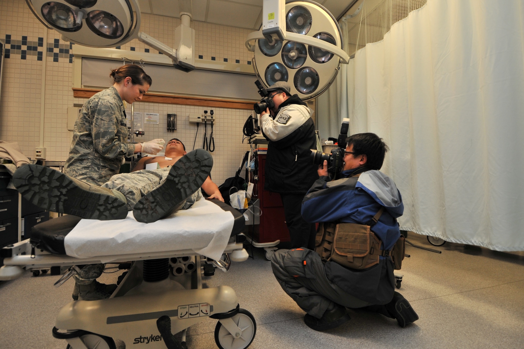 Photojournalists from the Defense Times Korea take photos of 1st Lt. Candice Milone, 8th Medical Support Squadron, as she dresses a wound at Kunsan Air Base, Republic of Korea, Feb. 10, 2012. Kunsan Airmen will be featured in the March issue of Defense Times Korea. (U.S. Air Force photo by Senior Airman Brittany Y. Auld/Released)