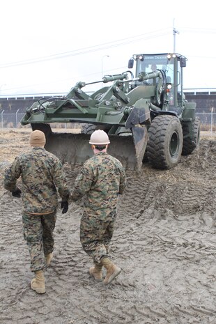 Lance Cpl. Seth A. Cozean, a Marine Wing Support Squadron 171 heavy equipment operator, and Seaman Joshua A. Silva, Headquarters and Headquarters Squadron utilities constructionman, look on as a John Deere TRAM 624KR Tractor, Rubber Tired, Articulated Steering, Multi-purpose vehicle prepares to clear away debris and sections of a demolished fence on the north side of the station near the future sight of the proposed civilian terminal. Along with demolition, Seabees help in auxiliary roles aboard the station, particularly the barracks.