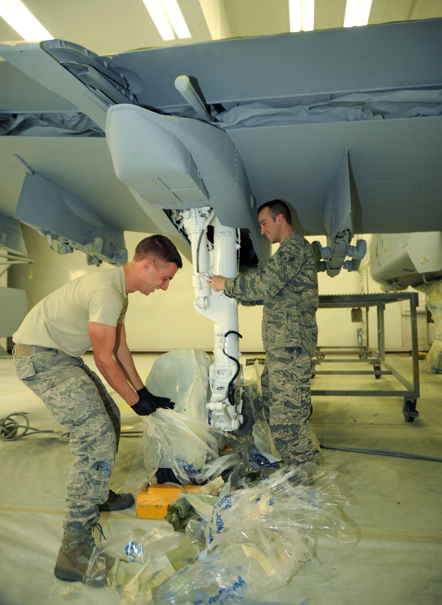 U.S. Air Force Airman 1st Class Andrew Lucas and Airman 1st Class Jonathan Hart, 355th Equipment Maintenance Squadron aircraft structural maintenance, remove tape, paper and sheets of plastic from around A-10 landing gear after painting the aircraft at Davis-Monthan Air Force Base, Ariz., Feb. 16. The whole process of painting one A-10 takes two weeks, one week to sand and one week to paint. (U.S. Air Force photo by Airman 1st Class Michael Washburn/Released)
